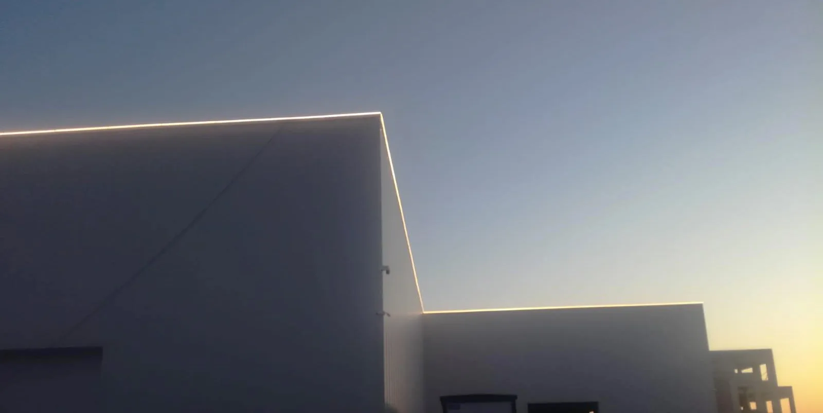 Alacakaranlıkta çatı hattı boyunca LED şeritle aydınlatılmış fabrika cephesi